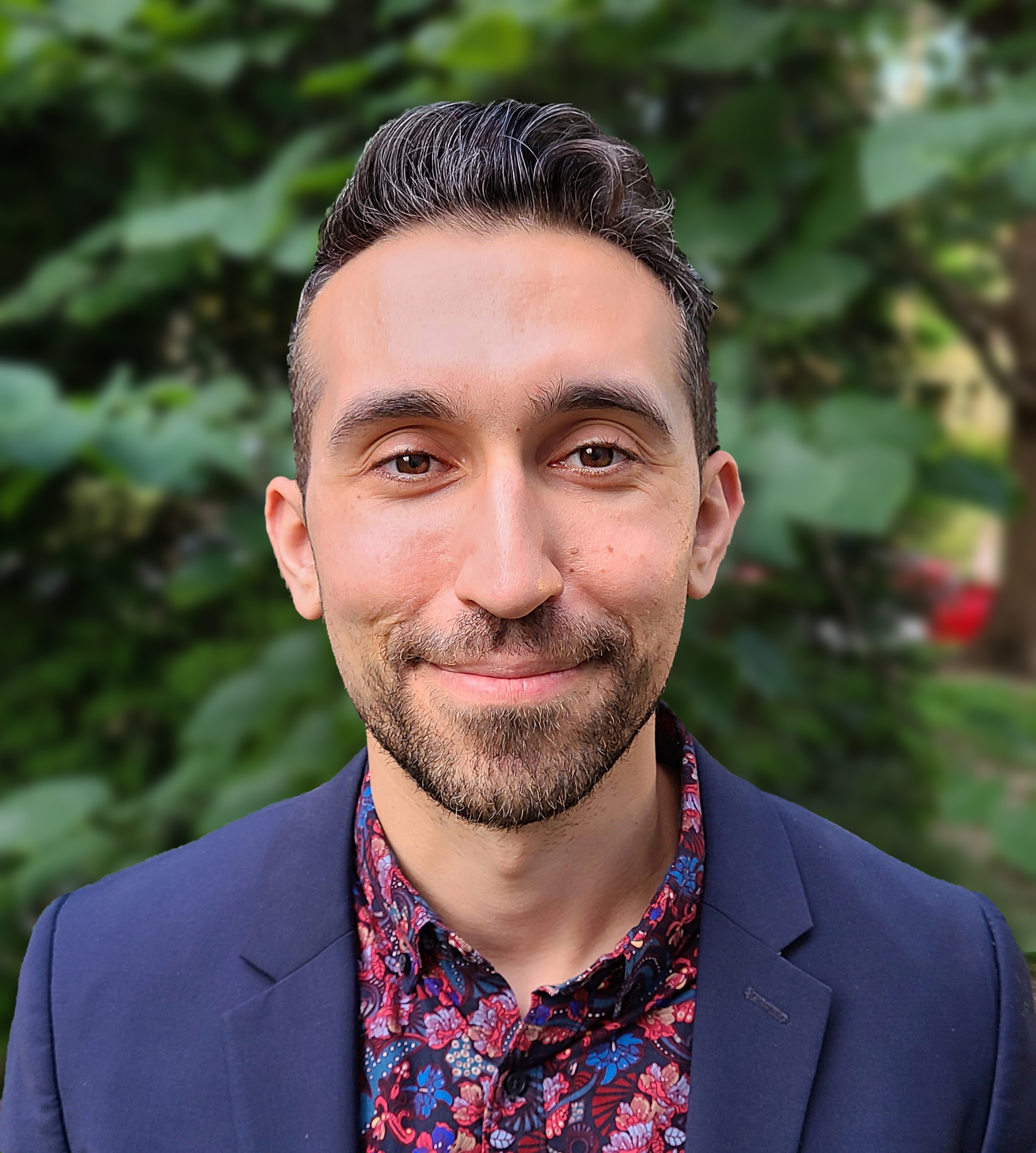 Associate Professor Daniel Aaron, a young man with olive skin and dark brown hair and a beard wearing a navy blazer and navy and fuchsia floral shirt