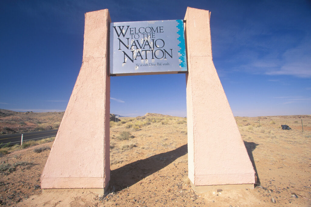 Concrete pillars with a metal sign in between that says "Welcome to the Navajo Nation" in a desert landscape